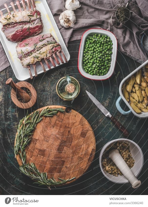Meat food background. Cooking preparation with raw lamb meat, green green peas , back potatoes and rosemary bread crust on rustic table with empty cutting board. Top view. Racks of lamb