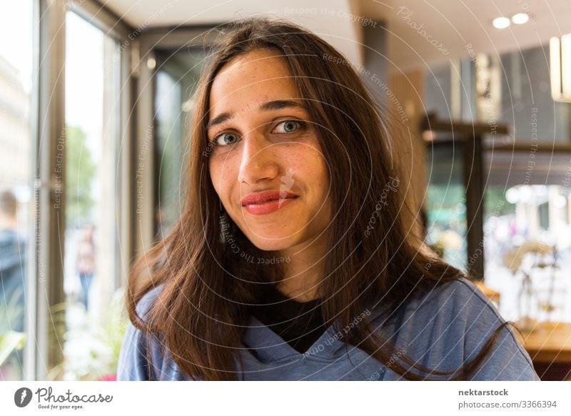 Portrait of Mixed Race Indian Girl Sitting in Coffee Shop female tanned skin light colored eyes smile looking at camera dark hair lipstick interior inside