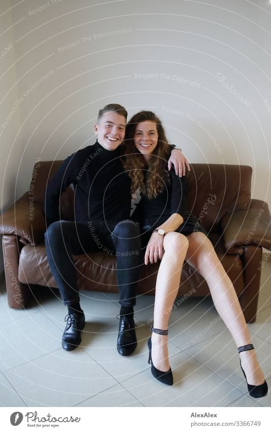 Young man and young woman sitting together on a brown leather couch and smiling Lifestyle Style Joy already Harmonious Living or residing Sofa Room Young woman