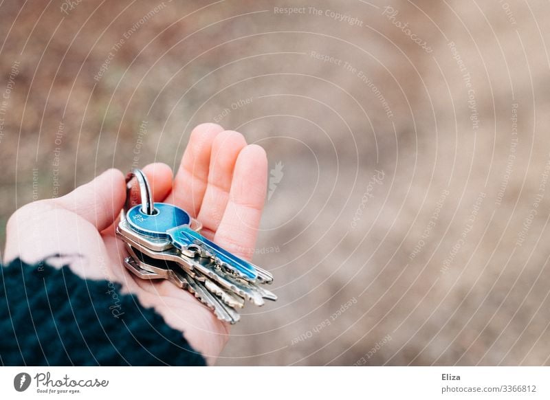 A hand that hands over a bunch of keys with a blue key on it when handing over the apartment after a move. Concept of living, living space and handing over the keys.