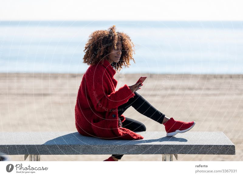 Beautiful afro woman sitting on shore using a mobile phone Style Happy Beach Telephone PDA Human being Feminine Young woman Youth (Young adults) Woman Adults 1