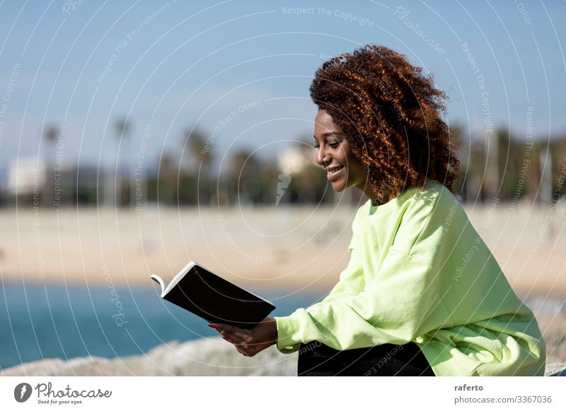 Side view of a afro woman sitting on shore reading a book Lifestyle Style Beautiful Reading Ocean Human being Feminine Young woman Youth (Young adults) Woman