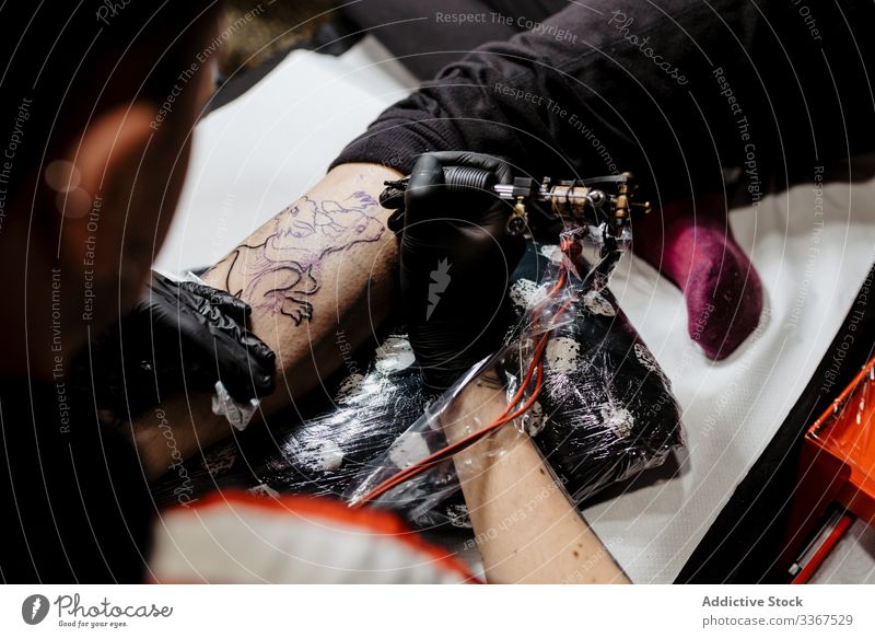Anonymous crop tattooist working with client in salon man tool stylish subculture artist master creative fashion professional tattooer modern contemporary