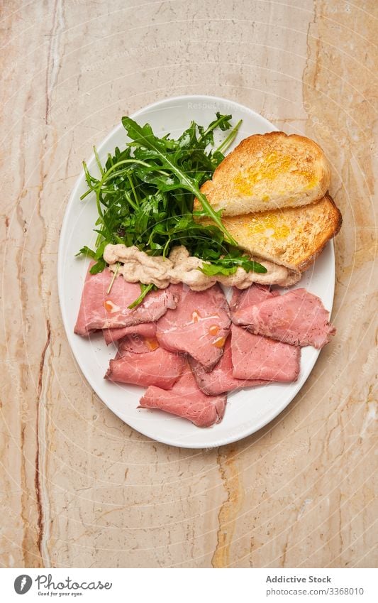 Tasty meat with bread and arugula dish plate ham jamon restaurant fresh green herb table wooden salad slice stylish elegant haute cuisine luxury rich savory