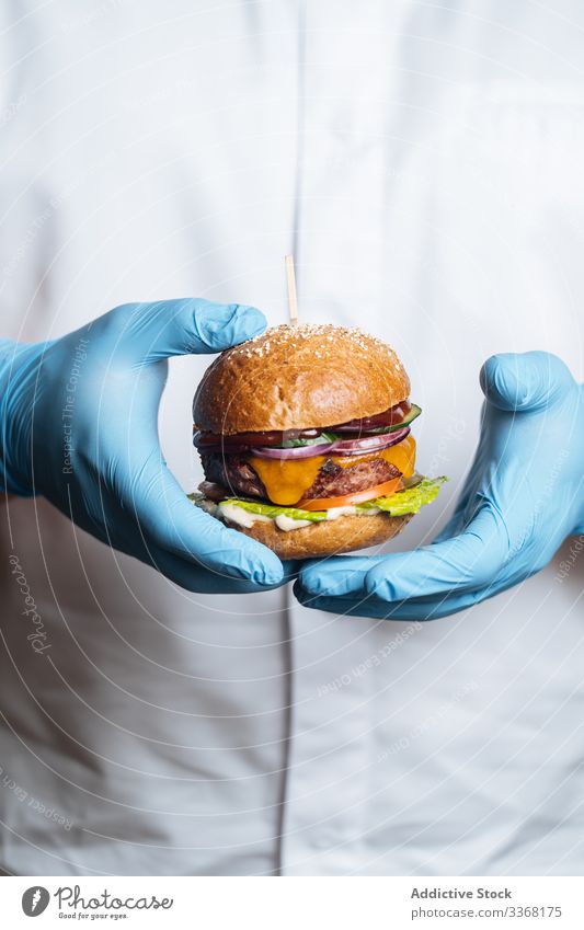 Anonymous person holding burger with fried patty and fresh vegetables fast food street food dish restaurant sauce onion lettuce venison cheese tomato meat salad