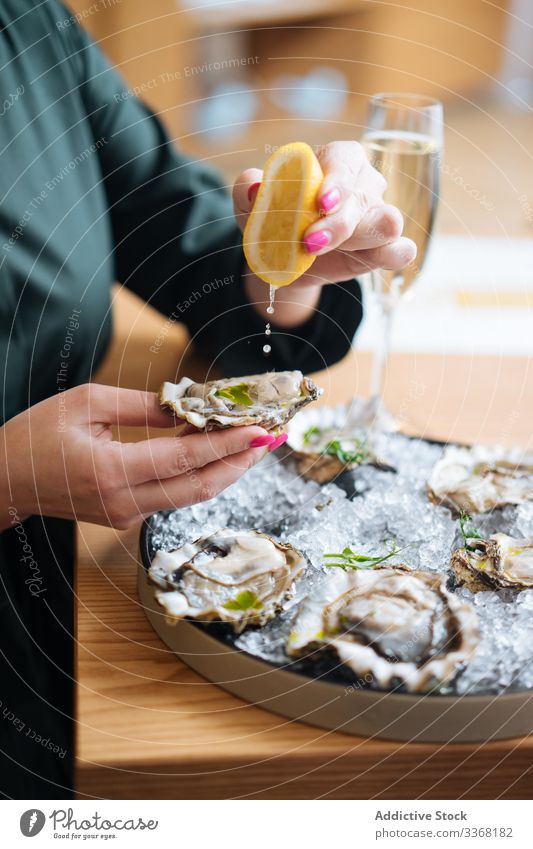 Crop person enjoying oysters and champagne eat drink restaurant lemon herb ice table clam seafood exquisite delicious tasty yummy palatable delectable savory