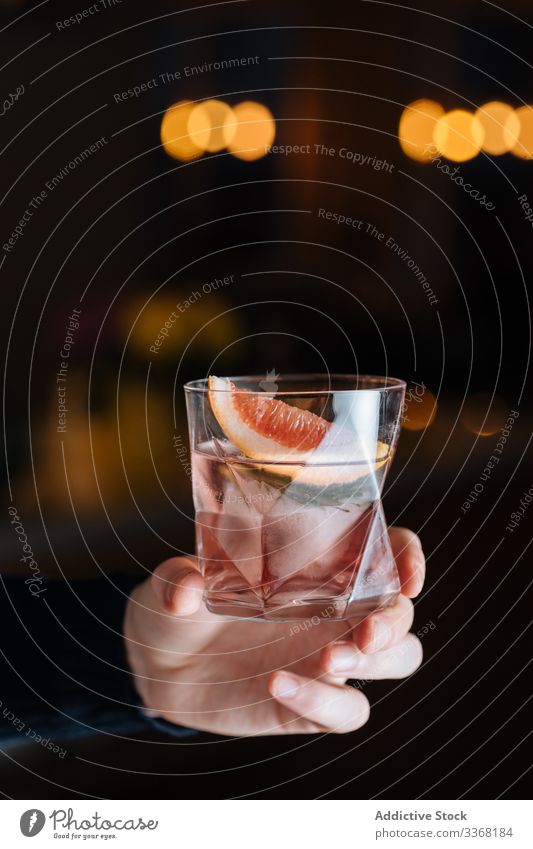 Anonymous person with alcoholic drink with sliced grapefruit and ice cocktail citrus bar table cup glass refreshment cold beverage cool party pub mixed soda