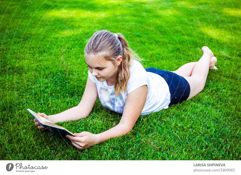 teenage girl lies on green grass and reads book in park Lifestyle Happy Beautiful Face Leisure and hobbies Reading Summer Garden School Study Human being Woman