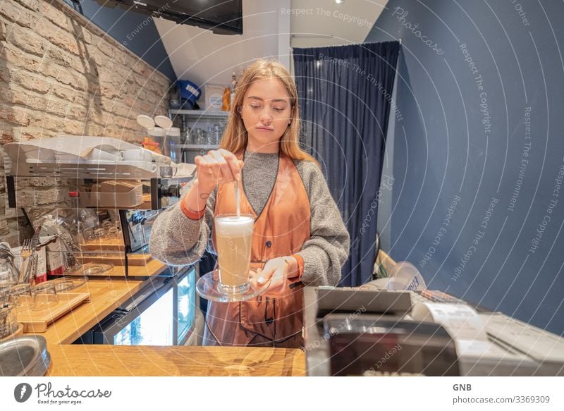 long lath Breakfast To have a coffee Beverage Hot drink Coffee Latte macchiato Glass Spoon Work and employment barista Workplace Café Human being Feminine
