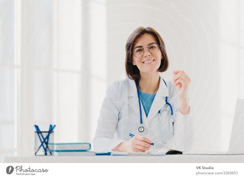 Young woman doctor writes on paper in clinic Happy Health care Medical treatment Medication Contentment Desk Table Work and employment Profession Doctor