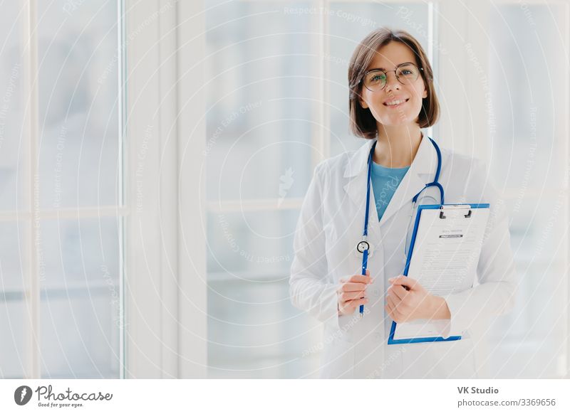 Beautiful intern holds clipboard with written papers and pen Happy Health care Medication Contentment Apprentice Work and employment Profession Doctor Hospital