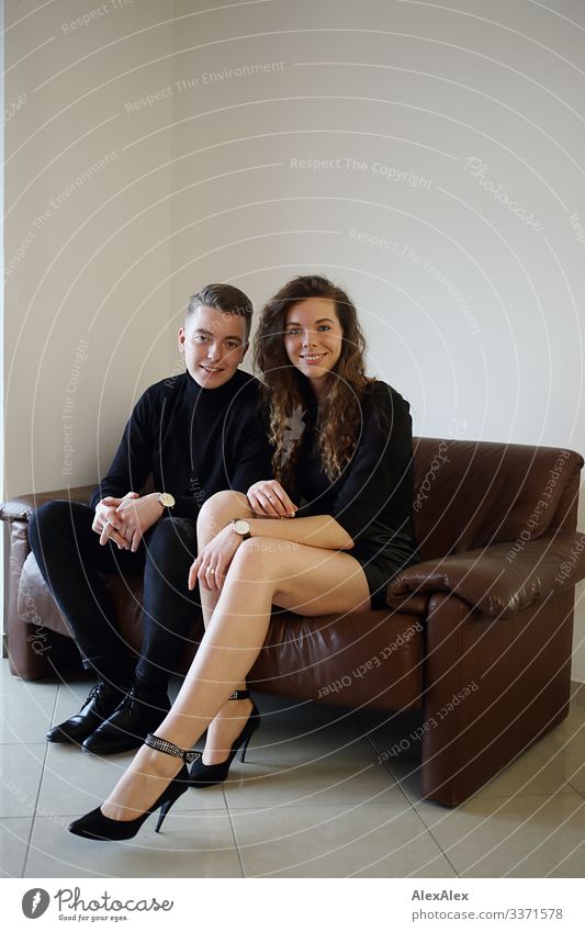 Young man and young woman sitting together on a brown leather couch and smiling Lifestyle Style Joy already Harmonious Flat (apartment) Sofa Young woman