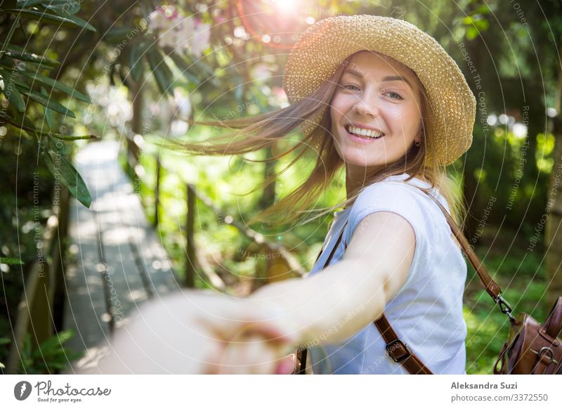 Beautiful woman in straw hat travel in tropic forest, walking along wooden path, leading her partner. Tourist with backpack. Follow me concept. active adventure