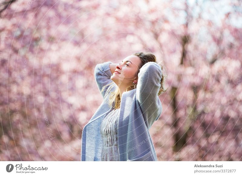 Young woman enjoying the nature in spring. Dancing, running and whirling in beautiful park with cherry trees in bloom. Happiness concept Beautiful