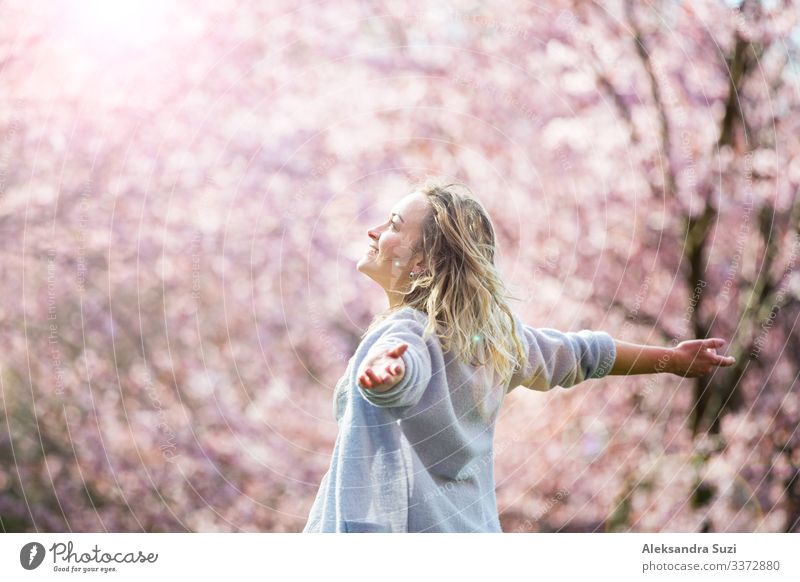 Young woman enjoying the nature in spring. Dancing, running and whirling in beautiful park with cherry trees in bloom. Happiness concept Beautiful