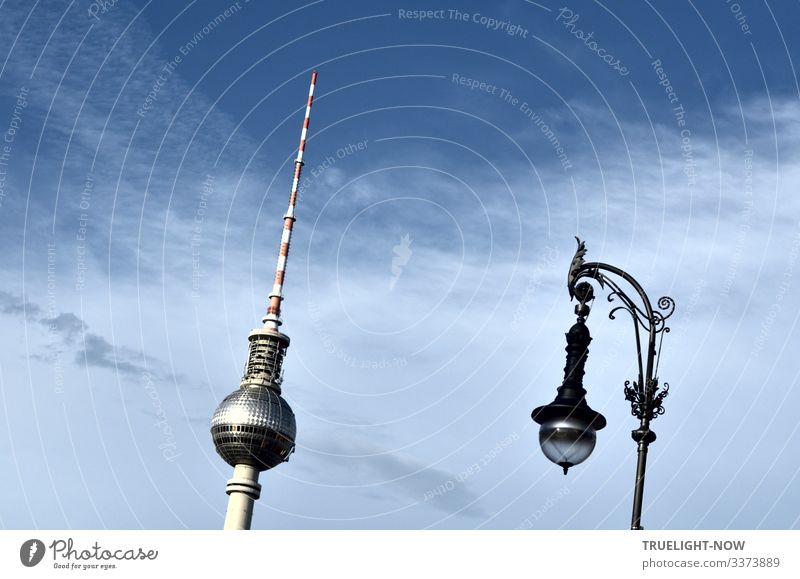 Berlin television tower at Alexanderplatz and street lamp in historical style parallel and reflecting the sunlight against the blue sky with partly light cloud cover