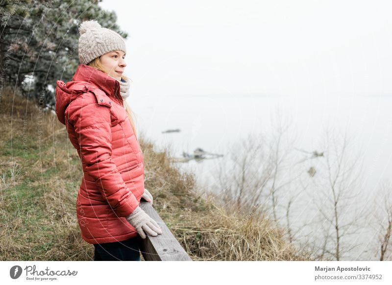 Young woman standing by the river in winter morning active adult adventure alone beautiful cap casual caucasian coast cold enjoying female free freedom frost