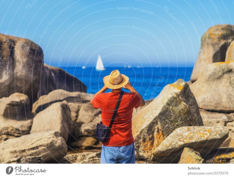 Tourist with straw hat in rear view photographs a sailing ship in Brittany at the sea between rocks Joy Leisure and hobbies Take a photo Vacation & Travel