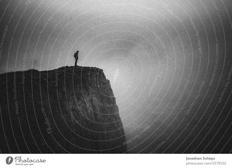 Young woman standing on a cliff in the fog Abstract Black Minimalistic Black & white photo Dark background Cliff Threat Dangerous Risk Dark gray Sombre mood