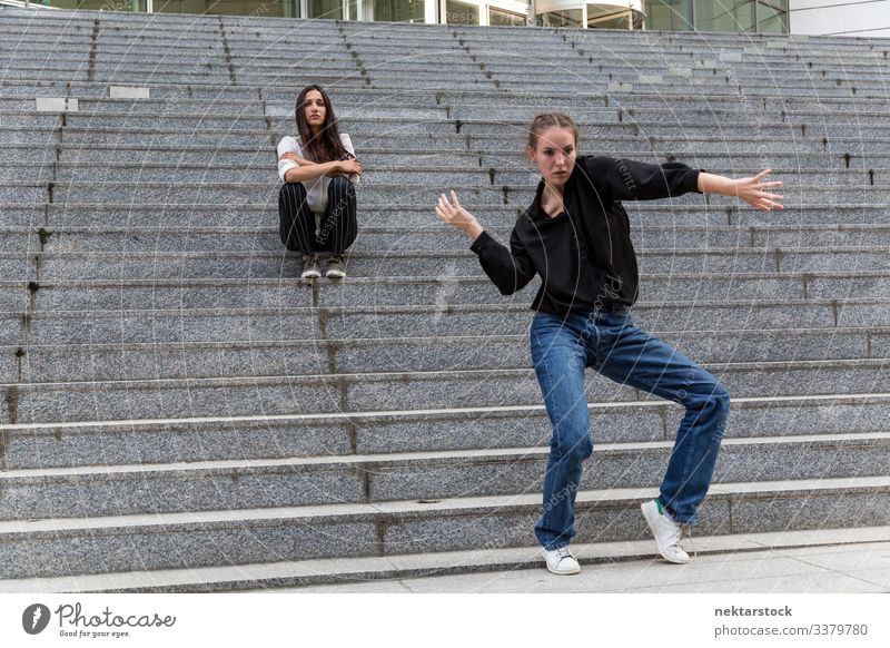 Young Woman Dancing and Another Sitting on Marble Steps sitting dancing females girl steps staircase women young adult youth culture day urban female beauty