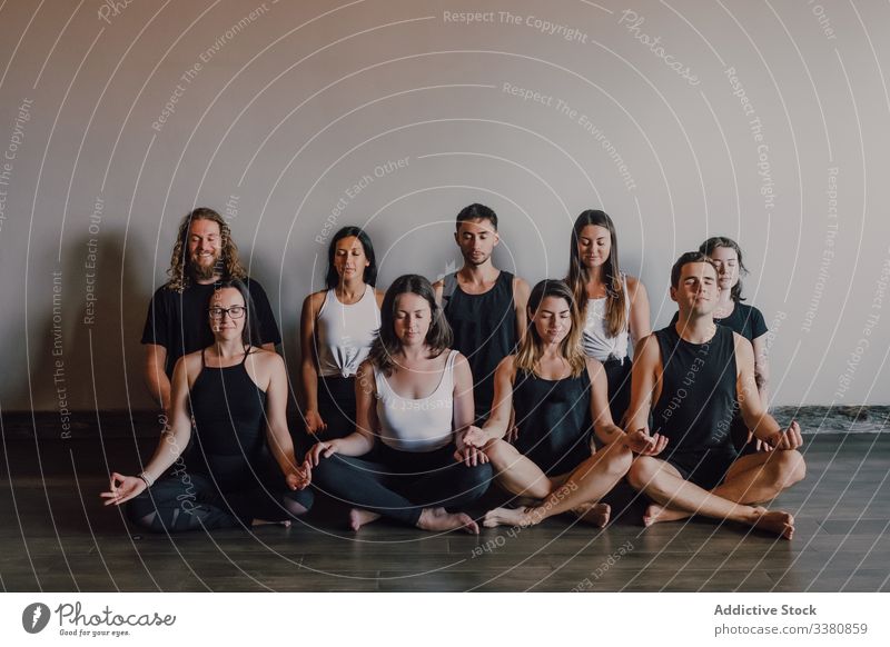 Group of calm relaxed athletes practicing yoga together performing lotus pose in light modern workout room meditate gyan mudra training serene peaceful
