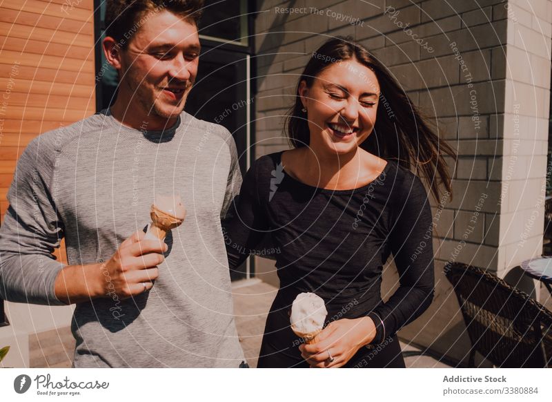 Cheerful relaxed couple laughing while leaving cafe and eating ice cream in summer sunny day cheerful street relationship date hug fun dessert cone positive