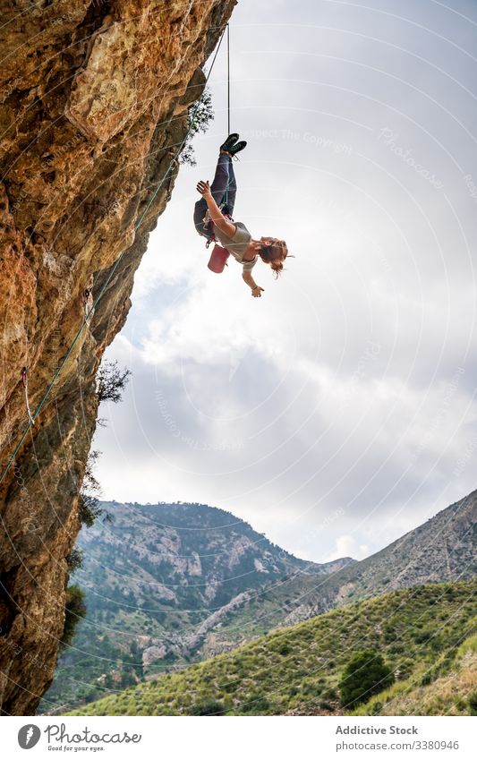 Brave female climber hanging upside down on cliff woman alpinist enjoy climbing adrenaline extreme challenge risk athlete freedom vacation danger height courage