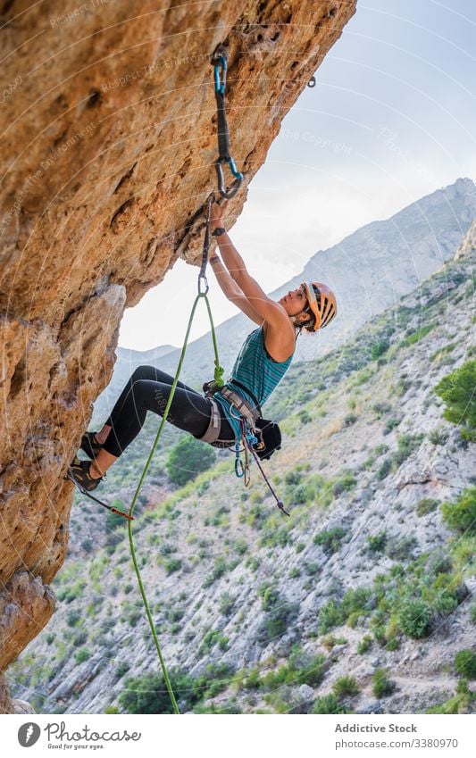 Concentrated young female climber ascending on cliff in summer woman alpinist mountain practice climbing active mountaineering risk travel brave adventure