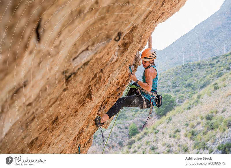 Concentrated young female climber ascending on cliff in summer woman alpinist mountain practice climbing active mountaineering risk travel brave adventure