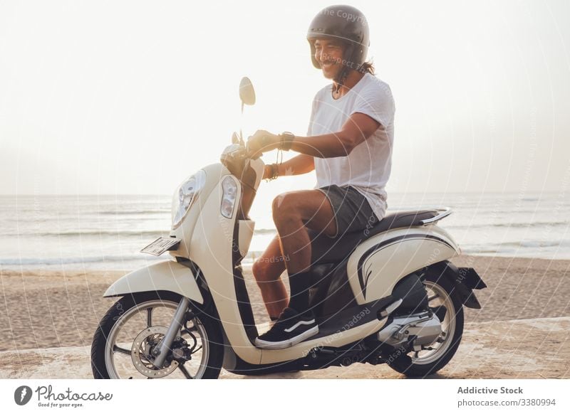 Cheerful biker on sandy beach man happy active smile sea summer ride scooter motorbike motorcycle male freedom travel journey helmet adventure drive vehicle