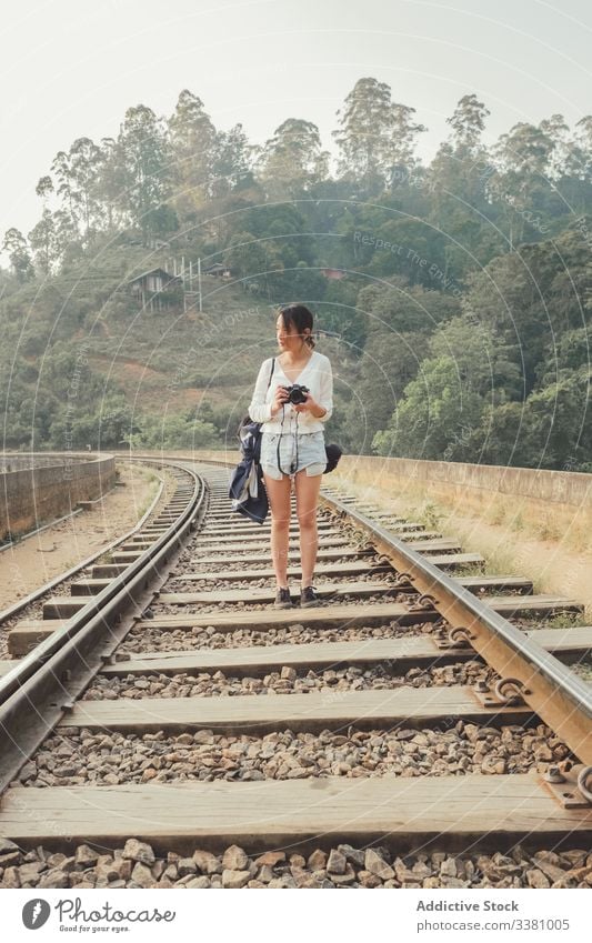 Female tourist walking on lonely railway against exotic forest woman take photo camera empty photography green bridge plant tourism travel nature lifestyle