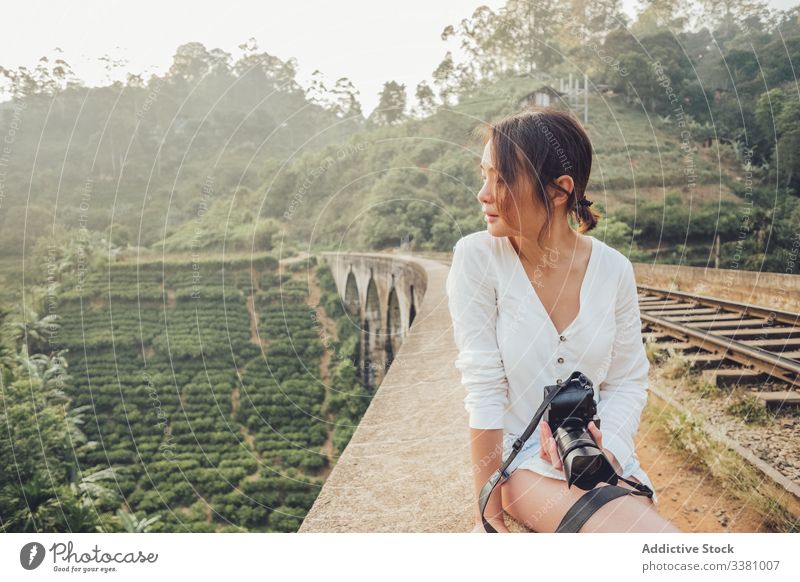 Young Asian woman on vacation taking photo with camera in nature tale photo travel exotic jungle railroad explore view tourism photography sit fence green plant