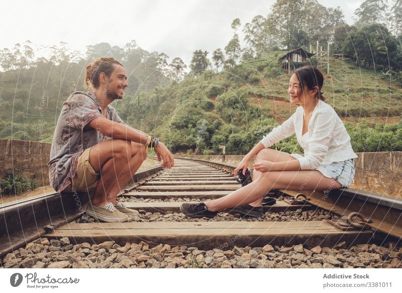 Woman shooting man with camera while sitting on railroad couple travel take photo tropical exotic together explore memory tourism rails freedom cheerful relax