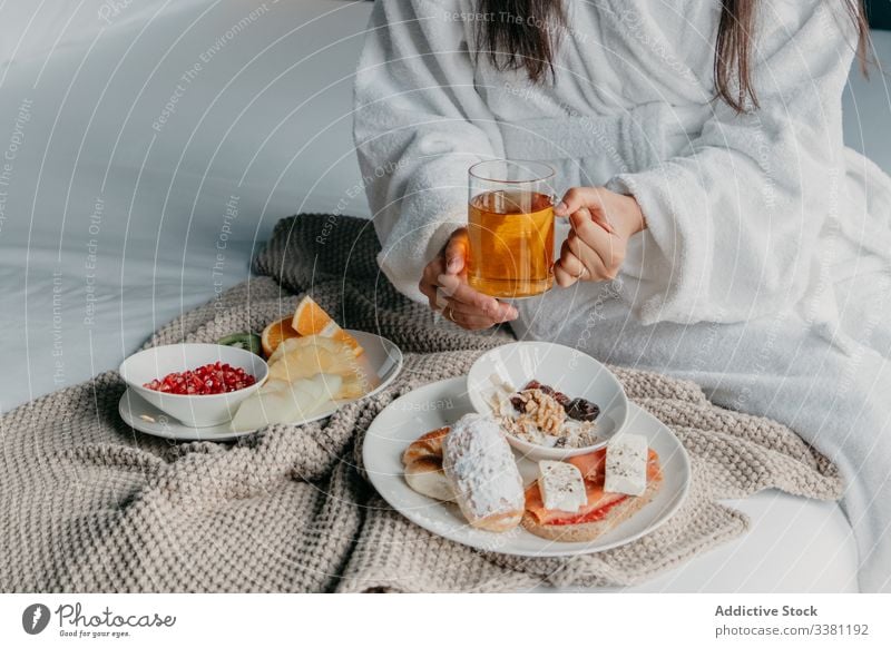 Anonymous woman having breakfast in bed tea happy bathrobe cheerful mug cup drink female food cozy tasty home relax fresh beverage morning delicious rest