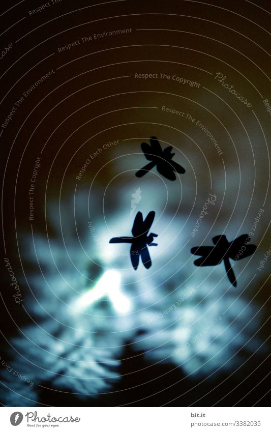 Dragonfly dance with cut out silhouettes of dragonflies made of clay paper, in front of a bright blue and black background. Point of light Hover Flying