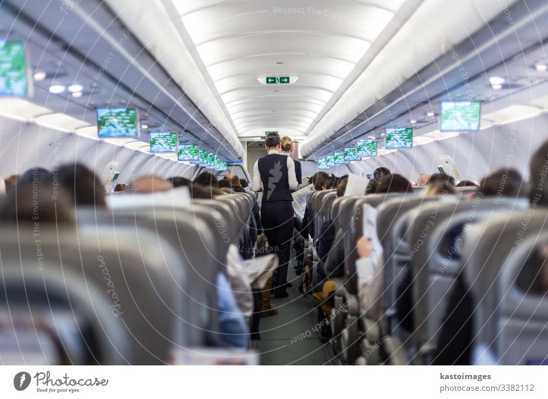 Interior of commercial airplane with stewardess serving passengers on seats during flight. flight attandant aeroplane aircraft interior cabin crowded transport