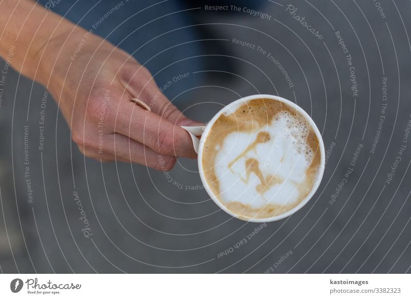 Hand holding a cup of coffee to go. latte paper art take away top view plastic drink disposable cappuccino cafe white work black break breakfast caffeine city