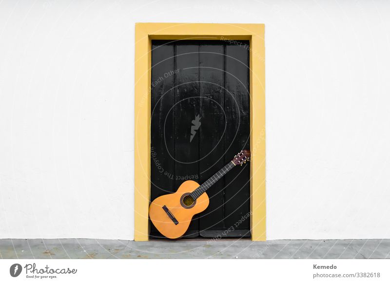 Spanish or classical guitar resting on a door of an andalusian patio. Outdoor scene of a musical instrument in the white wall of a rural house. flamenco spanish