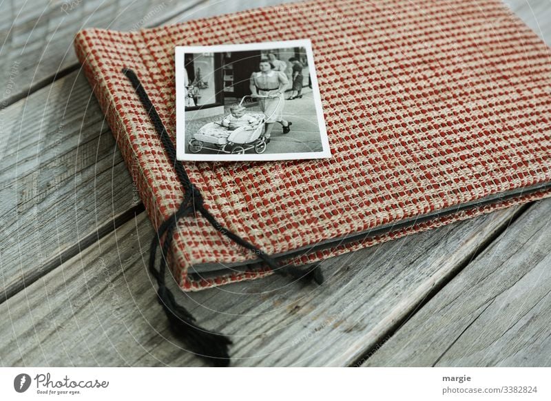 An old photo album lies on a wooden table. A photo with a mother pushing a baby carriage with a toddler. Photography Photo album Wooden table Baby carriage