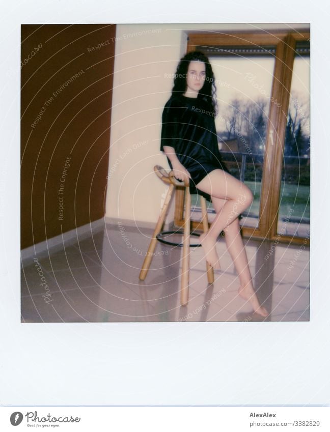 Young woman sitting on a chest of drawers in front of a yellow