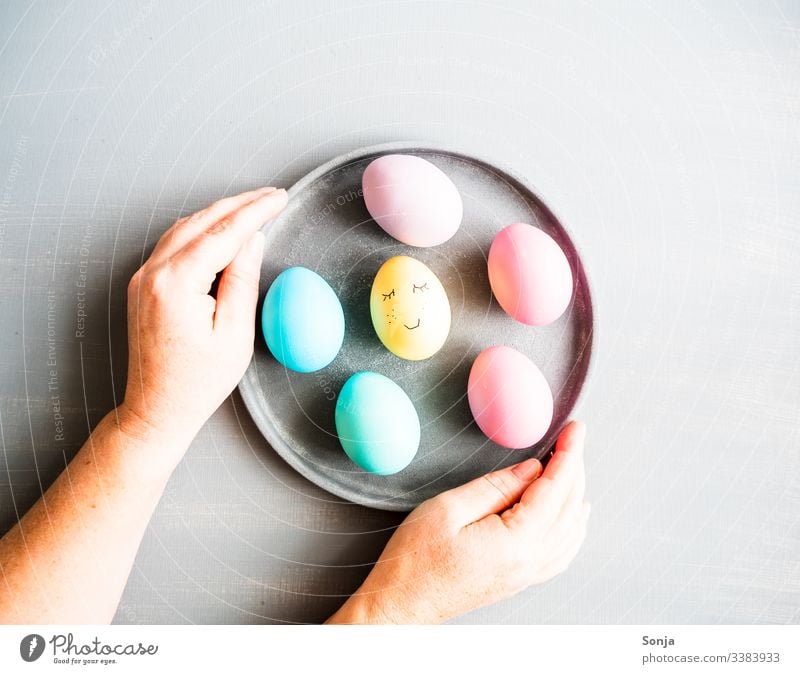 Hands holding a plate of Easter eggs Painted Woman Table Gray plan painted face Humor Funny Plate stop Egg pastel shades Food photograph Protein Anticipation