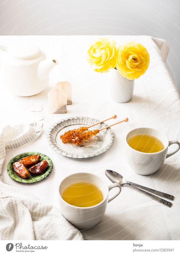 Kräutertee mit gelben Blumen auf einem weißen Tischtuch kräutertee heiß teekanne teebeutel kandiszucker teepause tischtuch weiss datteln getränk frühstück