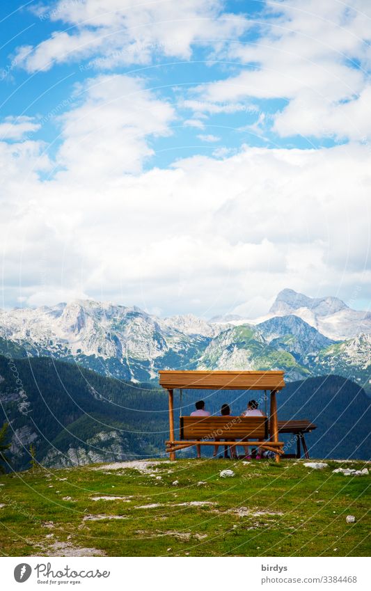 Tourists sit on a bench or swinging seat on the top of the mountain Vogel in Slovenia and marvel at the Alpine panorama in front of them . in the border triangle Slovenia - Austria and Italy. Ski area Vogel, Slovenia