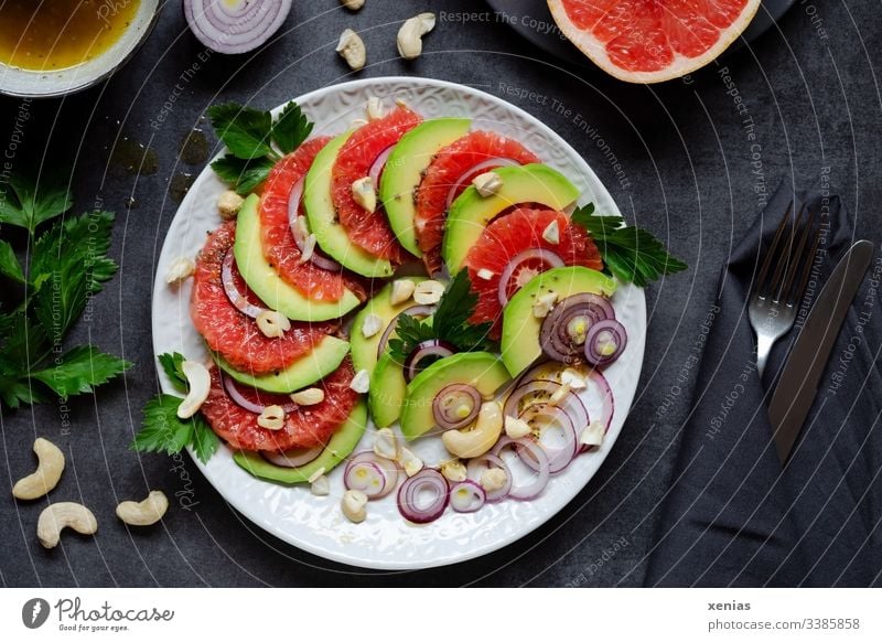 Salad with avocado, grapefruit, onions, cashew nuts and parsley served on a white plate with knife and fork in black napkin on a dark table Lettuce Grapefruit