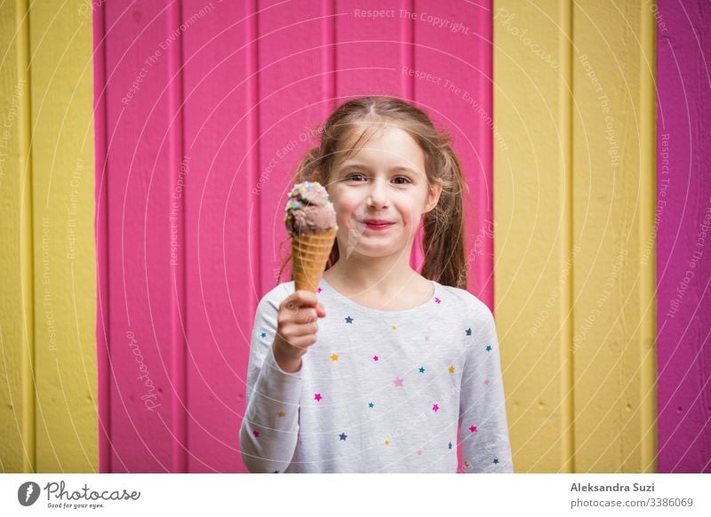 Cute little girl eating chocolate ice cream. Smiling and laughing. Colorful pink and yellow wall on background. Bright summer concept beautiful bright cafe