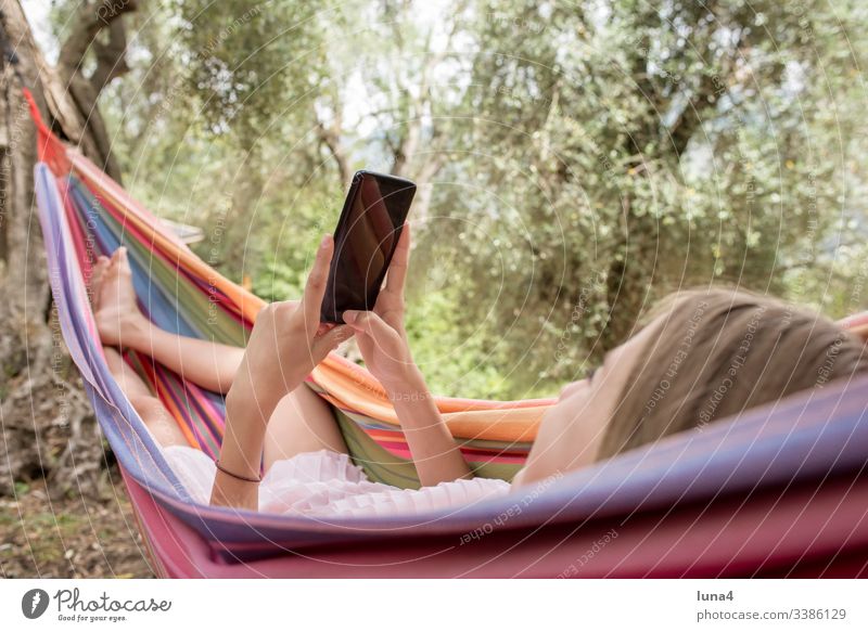 Girl with smartphone lying in hammock Hammock Cellphone vacation cheerful holidays Lie recover rest Smiling reachability Nature fortunate Laughter Joy Internet