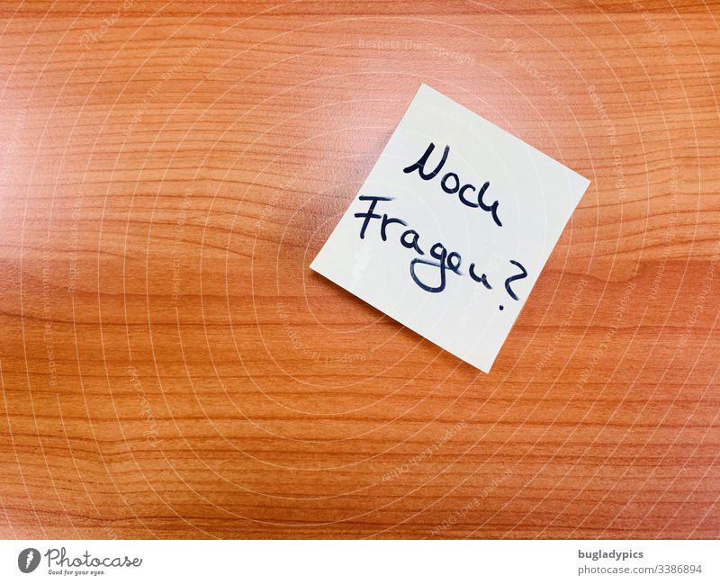 Smooth wooden surface with Post-It top right with text "Still questions? background Wood wood surface Piece of paper note Ask Question mark Communicate