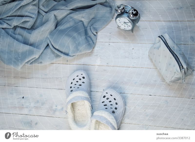 grey blanket with slippers, alarm clock and make-up bag on white wooden floor Blanket dwell at home Living or residing Shades of grey House slippers Slippers