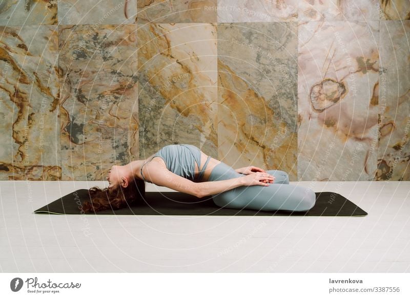 Young yogini practicing Matsyasana pose in pastel blue leggins and top, selective focus active athlete athletic attractive body brunette calm caucasian exercise