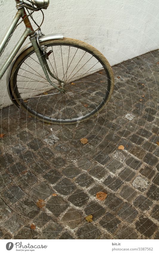 alt l old, nostalgic wheel in retro style, parked in front of a white, bright house wall on cobblestone. front part, lamp, light, tyre of grey wheel parked in the city.danger of theft of old bike, unsecured, not locked in autumn